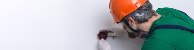 An electrician installs sockets in the apartment A guy in an orange helmet and overalls makes electrics in the house