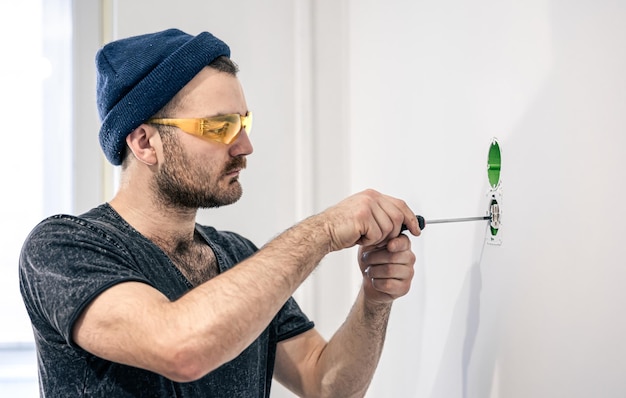 An electrician is mounting electric sockets on the white wall indoors