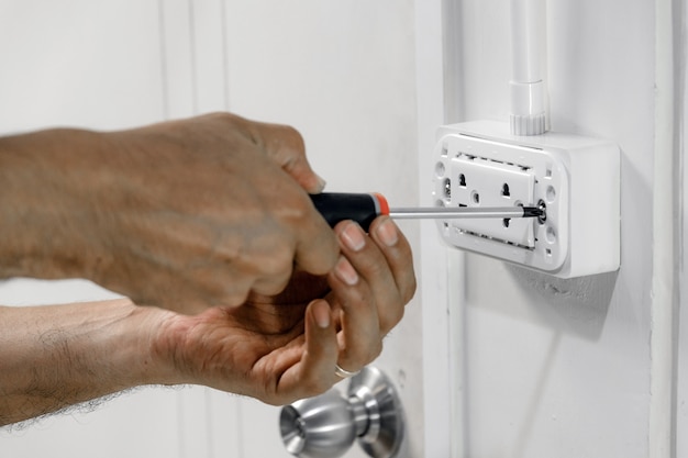 The electrician is using a screwdriver to attach the power cord to the wall outlet.