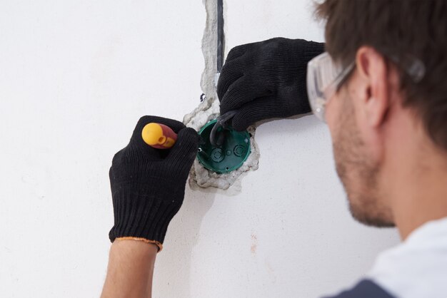 Electrician man instalation socket for wiring in concrete wall.