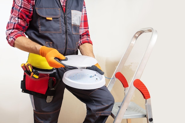 Uomo dell'elettricista che installa la lampada da soffitto elettricista al lavoro che ripara la lampada