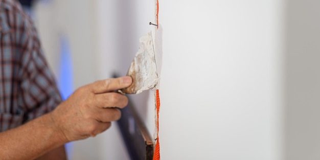 Electrician plastering orange corrugated wire into a wall in an electrical circuit constrauction image