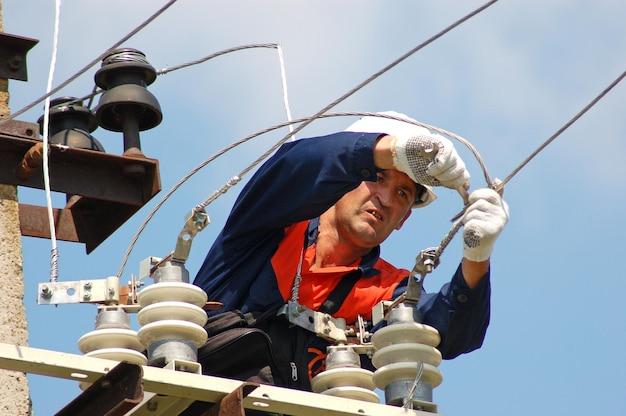 An electrician repairs a broken wire on an overhead power line