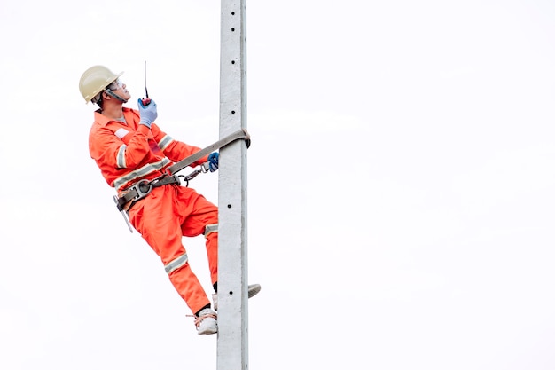 An electrician in a safety suit is climbing a light pole