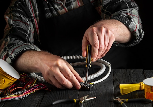 Electrician screws the wire to connector with screwdriver. Close-up of the hands of the master in workshop