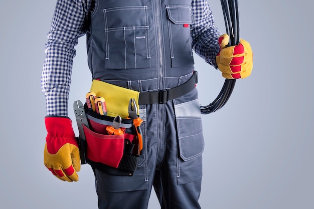 Foto elettricista in uniforme con fili sulla superficie grigia.