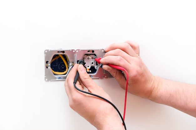 Electrician a wall socket with electronic multimeter. Wire and multimeter in hands close up