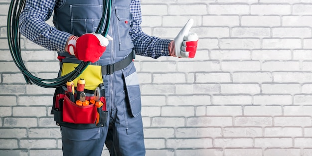 Elettricista con fili e utensili elettrici vicino a un muro di mattoni, spazio per il testo. bandiera.