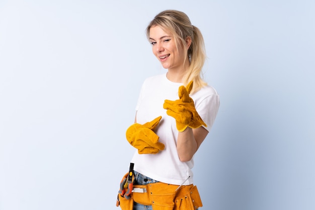 Electrician woman over isolated blue points finger at you