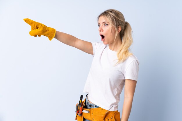 Electrician woman over isolated blue wall pointing away