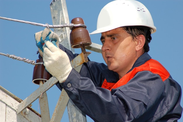 An electrician works on an electric pole to replace an electrical insulator