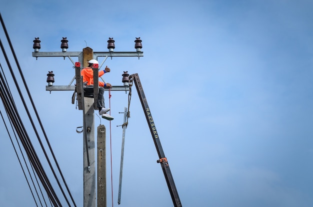 電気技師は、送電線の設置と修理のために電柱に登っています。