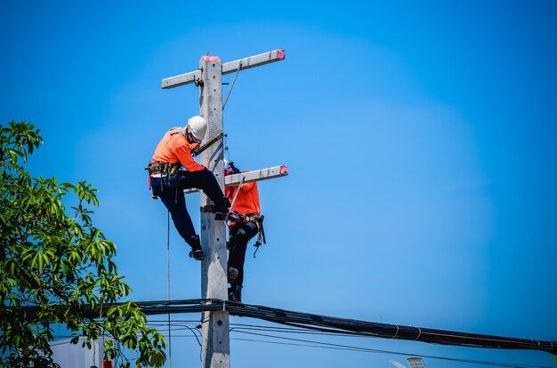 電気技師は、送電線の設置と修理のために電柱に登っています。