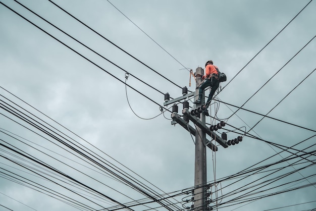 電気技師は、送電線の設置と修理のために電柱に登っています。