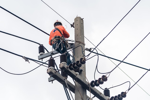 電気技師は、送電線の設置と修理のために電柱に登っています。