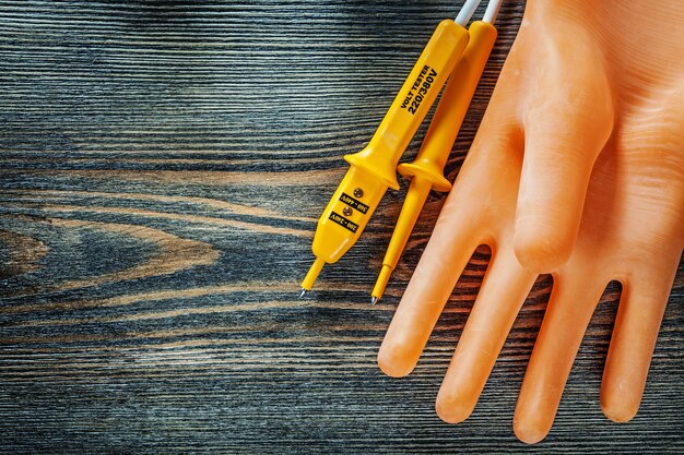 Electricians gloves electric tester on wooden board.