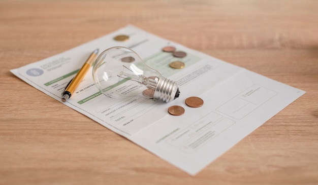 Electricity bill with light bulb several coins and pen on the desk Concept of electricity prices and tax payments