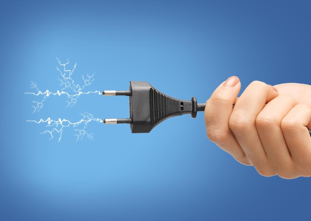 Photo electricity concept - close up of hand holding black electrical plug with wire