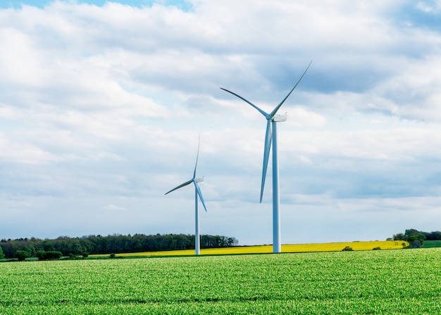 An electricity generating windmills on the yellow and green field against cloudy blue sky in England