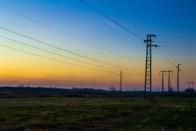 Electricity pylon on field against sky at sunset