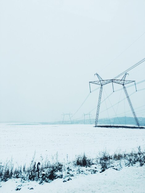 Electricity pylon on snow covered field against sky