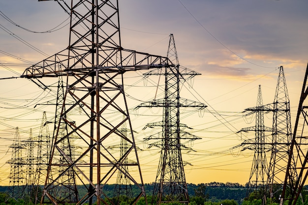 Electricity pylons bearing the power supply across a rural landscape during sunset. Selective focus.