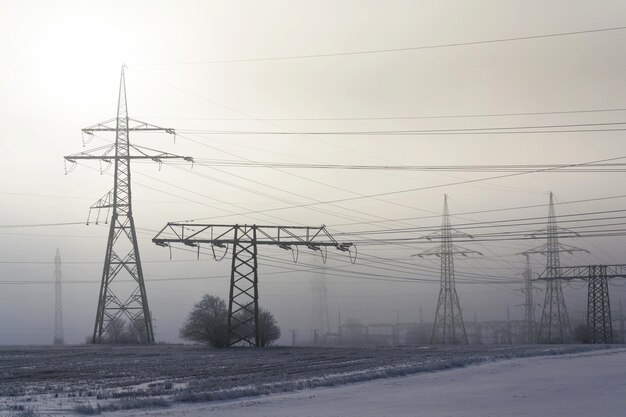 Electricity pylons from distribution power station in foggy winter freeze