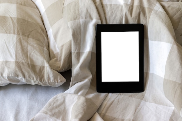 Electronic book with a blank screen on a white and beige bed