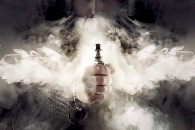 Electronic cigarette in hand in the middle of thick smoke