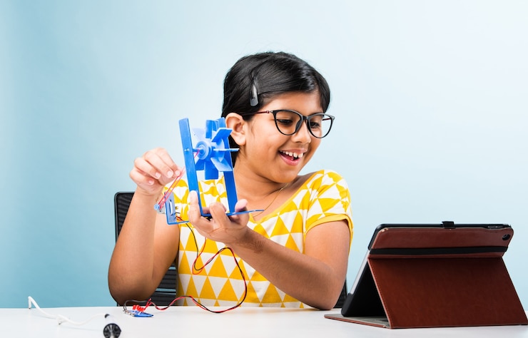 फोटो electronic experiment - asian indian small girl student performing windmill research with wires, connections, studying from laptop or tablet computer
