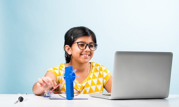 電子実験-ワイヤー、接続、ラップトップまたはタブレットコンピューターからの勉強で風車の研究を行うアジアのインドの小さな女の子の学生