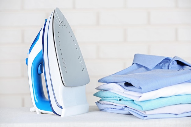 Electronic ironing and pile of clothes on board on brick wall background