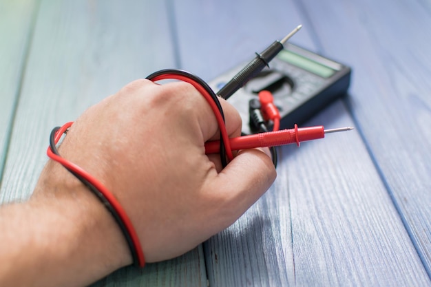 Electronic multimeter to measure the current in a male hand on a wooden background