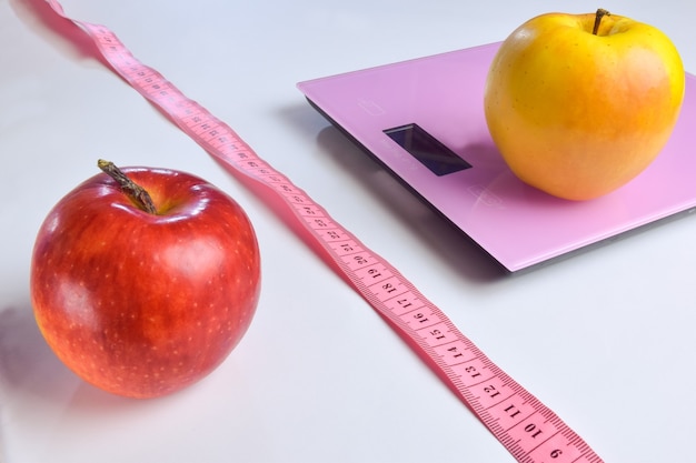 전자 저울 옆에는 두 개의 빨간색과 노란색 사과가 있고 그 옆에는 흰색 클리핑 배경에서 허리를 측정하기 위한 측정값이 있습니다.