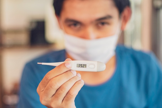 Foto termometro elettronico nella mano uomo che indossa la maschera bianca viso, contro il coronavirus. sintomi covid-19, temperatura elevata, tosse secca.