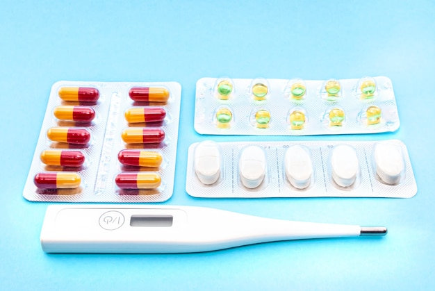 電子温度計と青いグラデーションの背景の健康概念の丸薬