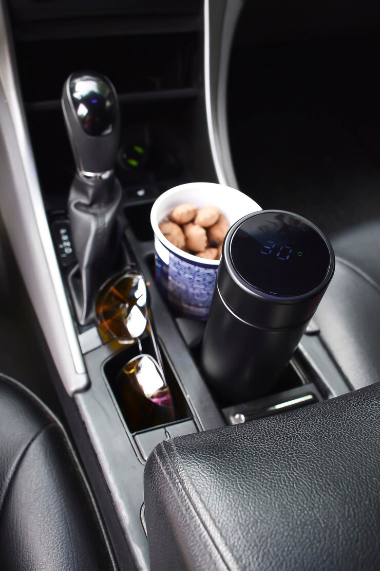 長いドライブの間に食べることを飲むために手の壊れた自動車の近くの車の内側のホルダーに置かれた紙ガラスのホットコーヒーティークッキースナックの電子魔法瓶