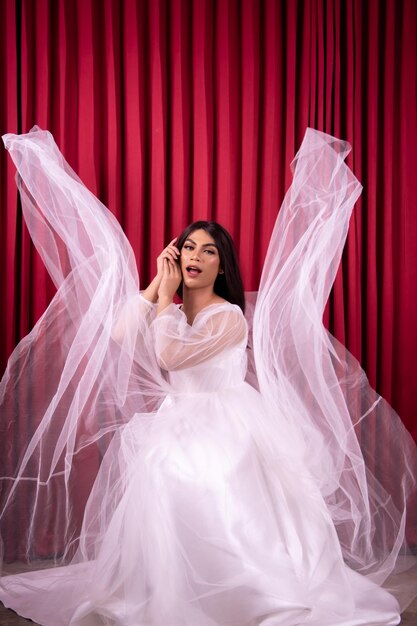 Elegance Asian woman wearing a wedding dress with flying fabric around her in front of the red curtain