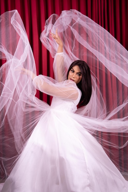 Elegance Asian woman wearing a wedding dress with flying fabric around her in front of the red curtain