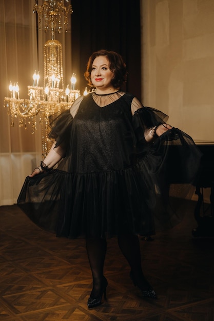 Photo an elegant adult woman in a black cocktail dress poses in the interior fashionable portrait of a woman