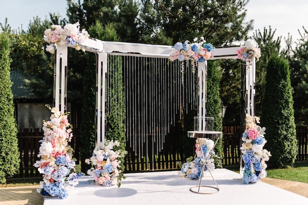 Elegant arch with fresh flowers on backyard Arch decorated pink roses and white blue flowers standing in the wedding ceremony area Wedding decor