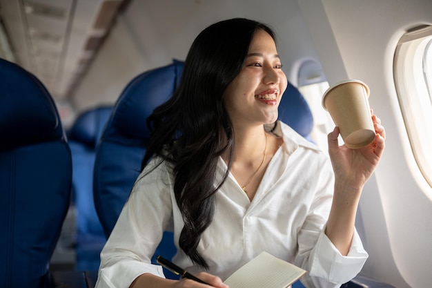 An elegant Asian businesswoman is sipping coffee while looking at the view outside the plane window