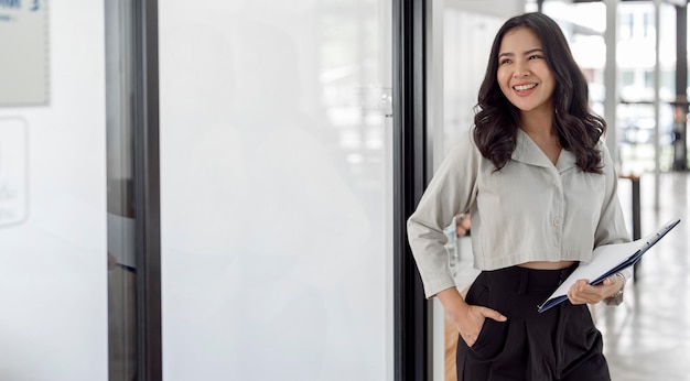 Elegante donna di affari asiatica in piedi nello spazio della copia dell'ufficio