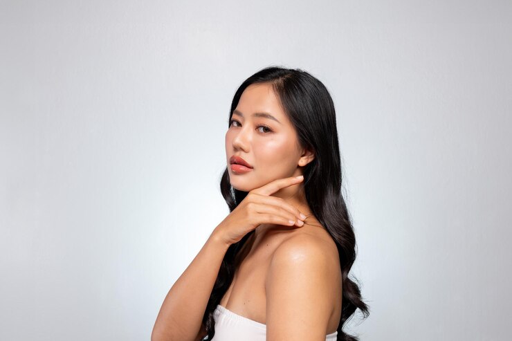 Photo elegant asian woman poses against a grey background looking at the camera while touching her chin