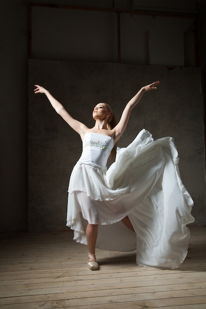 Фото Элегантная балерина в белых танцах с раскинутыми руками и развевающейся юбкой в студии