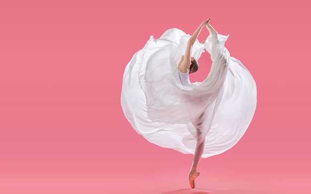 Элегантная балерина в пуантах танцует в длинной белой юбке на розовом фоне