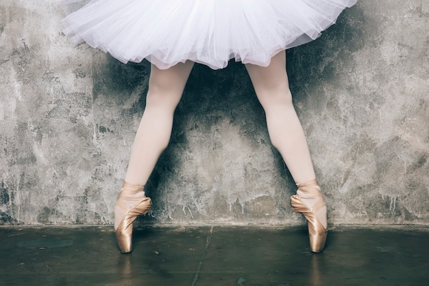 Elegant ballerina in white dress dancing against rustic wall