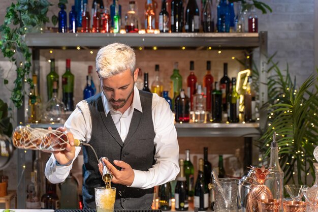 Элегантный бармен делает коктейль Мохито в ночном клубе, добавляя ингредиенты и создавая экспертные напитки на прилавке бара.