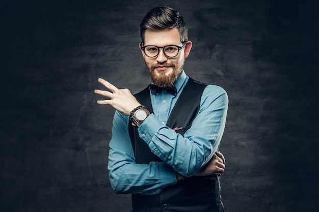 An elegant bearded hipster male dressed in a blue shirt and waistcoat over grey vignette background.