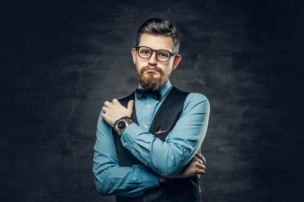 An elegant bearded hipster male dressed in a blue shirt and waistcoat over grey vignette background.